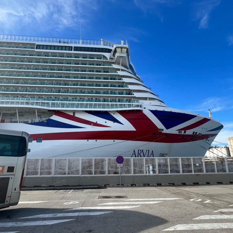 A large cruise ship with a Union Jack design docked at a port under a clear blue sky.