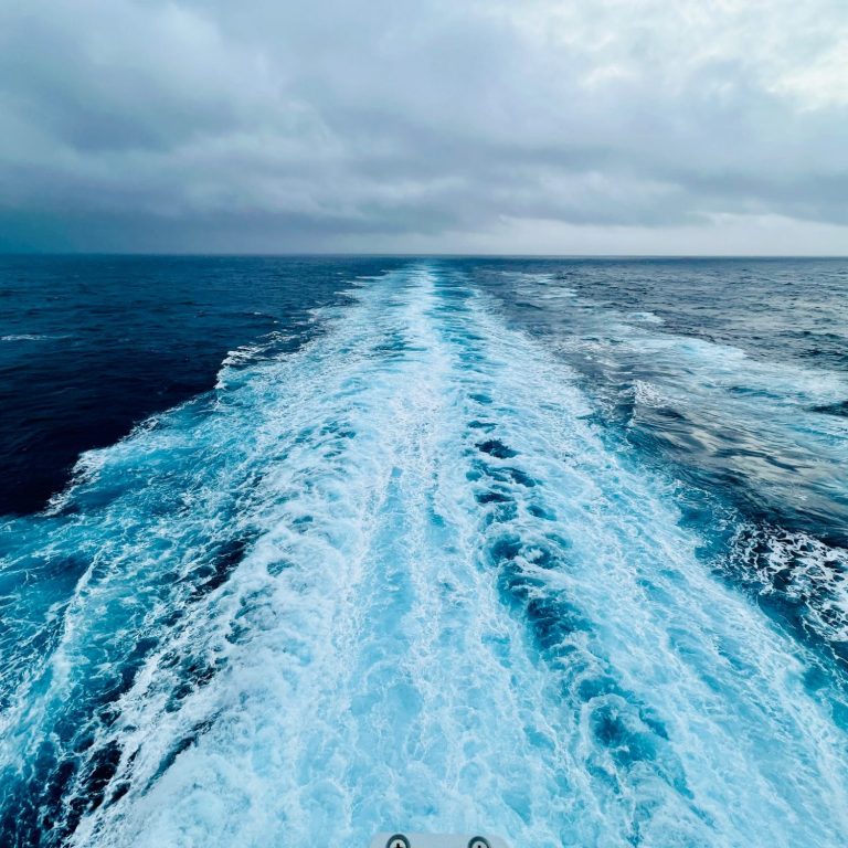 Waves and wake trailing behind a boat on a vast, cloudy ocean.